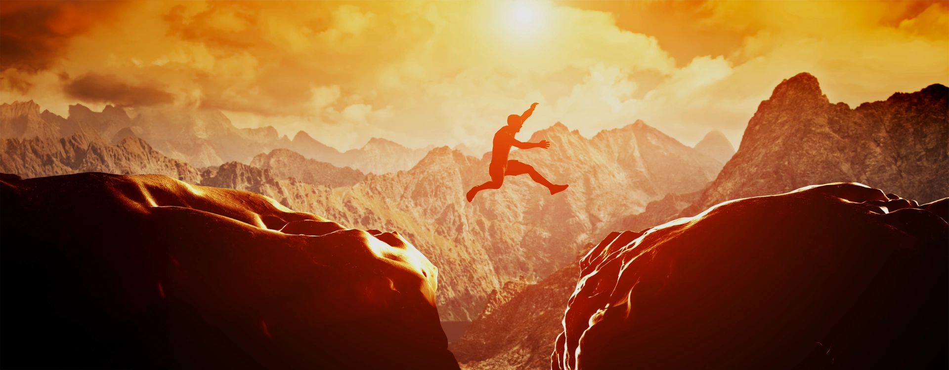 Man jumping from one cliff to another on a mountain at sunset